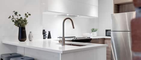 Une cuisine moderne dotée d’un îlot central, d’appareils électroménagers en acier inoxydable et de tabourets de bar.