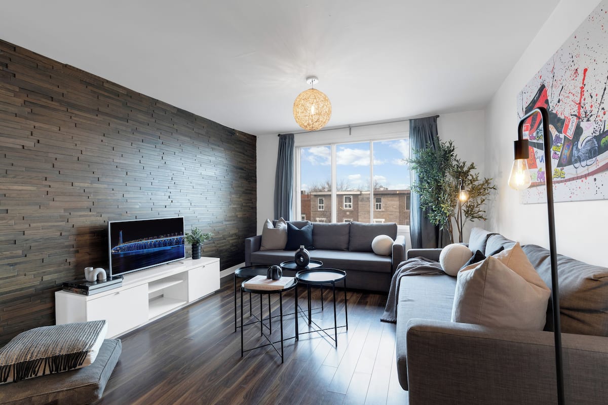 A modern living room with a flat-screen TV, a sofa, a coffee table, and a decorative light fixture.