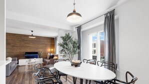A modern living room with a dining area, wooden wall, large windows, and a TV. - LiV MTL - Soho (Montreal)