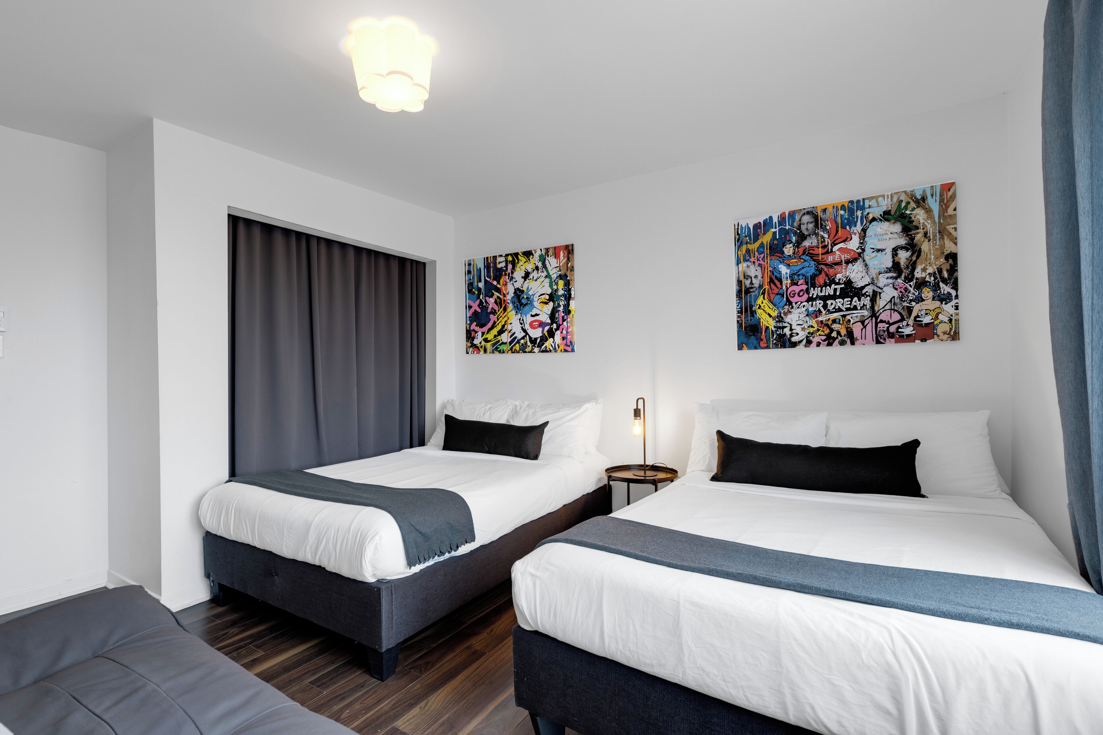 Ein Hotelzimmer mit zwei Betten, einem großen Fenster mit Vorhängen und zwei Wandbildern.