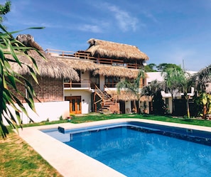 A two-story building with a thatched roof, a swimming pool, and a well-maintained garden. - Hotel el Risco (San Pedro Pochutla)
