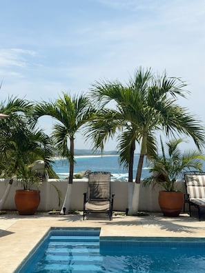 Un espace aménagé au bord de la piscine, avec une chaise et des plantes en pot, donnant sur une plage.