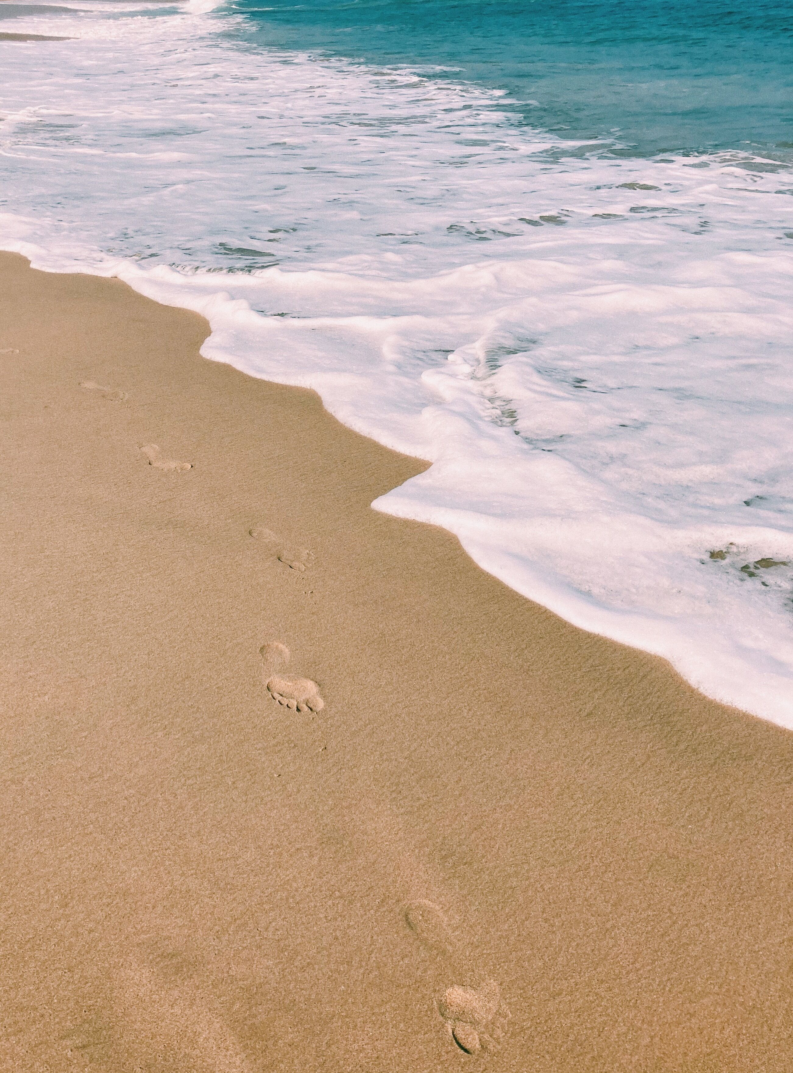A sandy beach with footprints leading to the water.