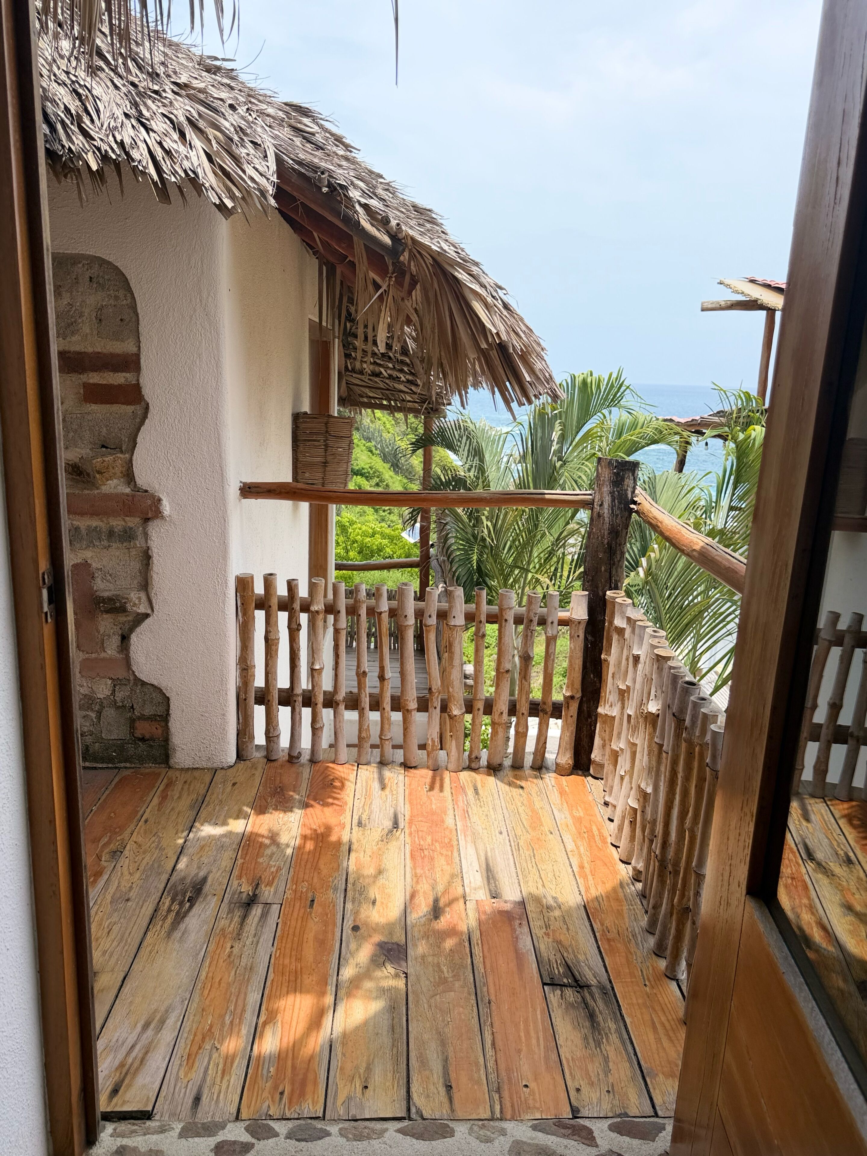 A wooden deck leading to a thatched-roof structure with a view of the ocean.