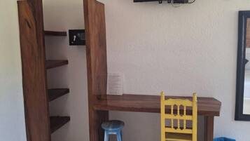 Una habitación con un escritorio de madera, un taburete azul, una silla amarilla, un televisor montado en la pared y un piso con diseño.