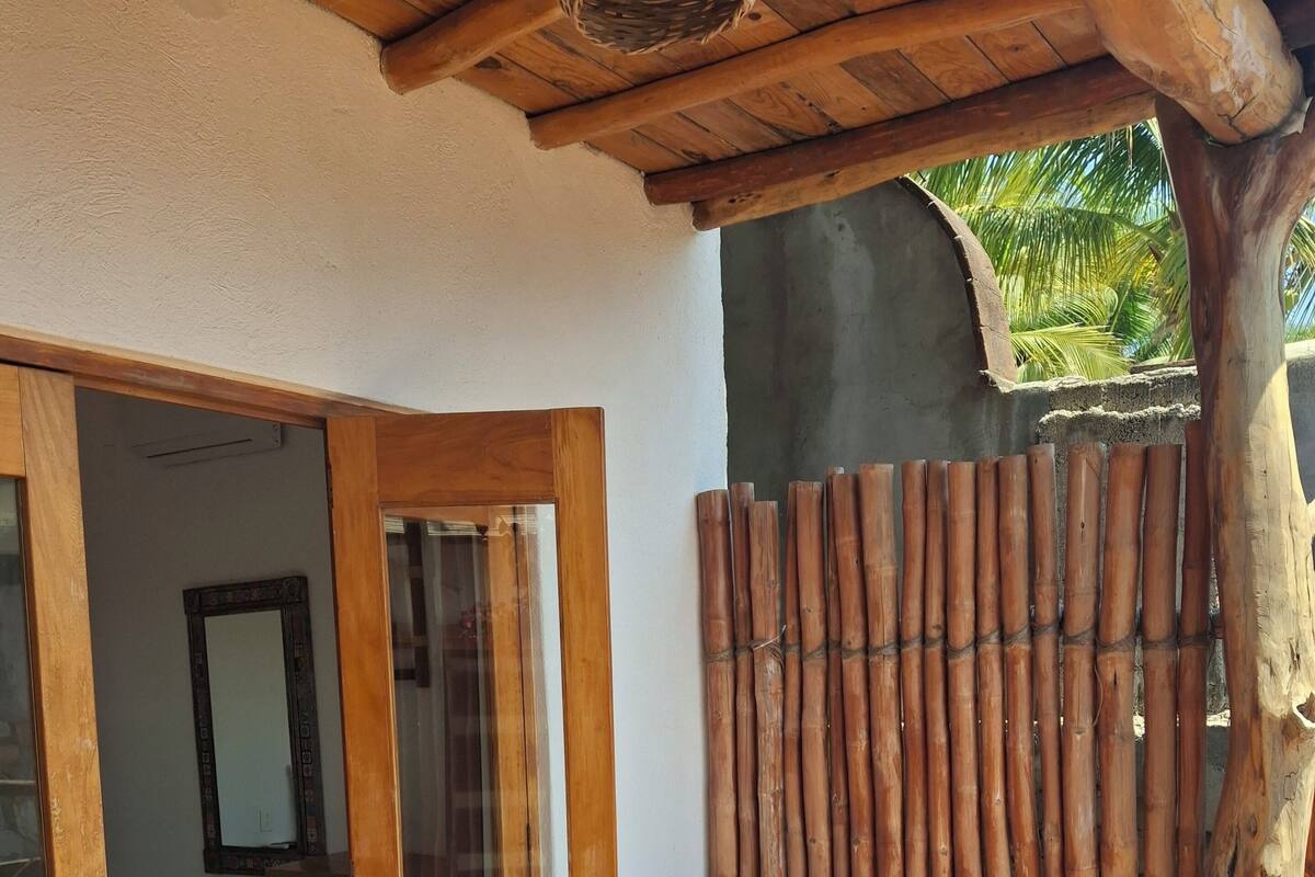 A wooden door leading to a room with a mirror, a white chair, and a bamboo fence.