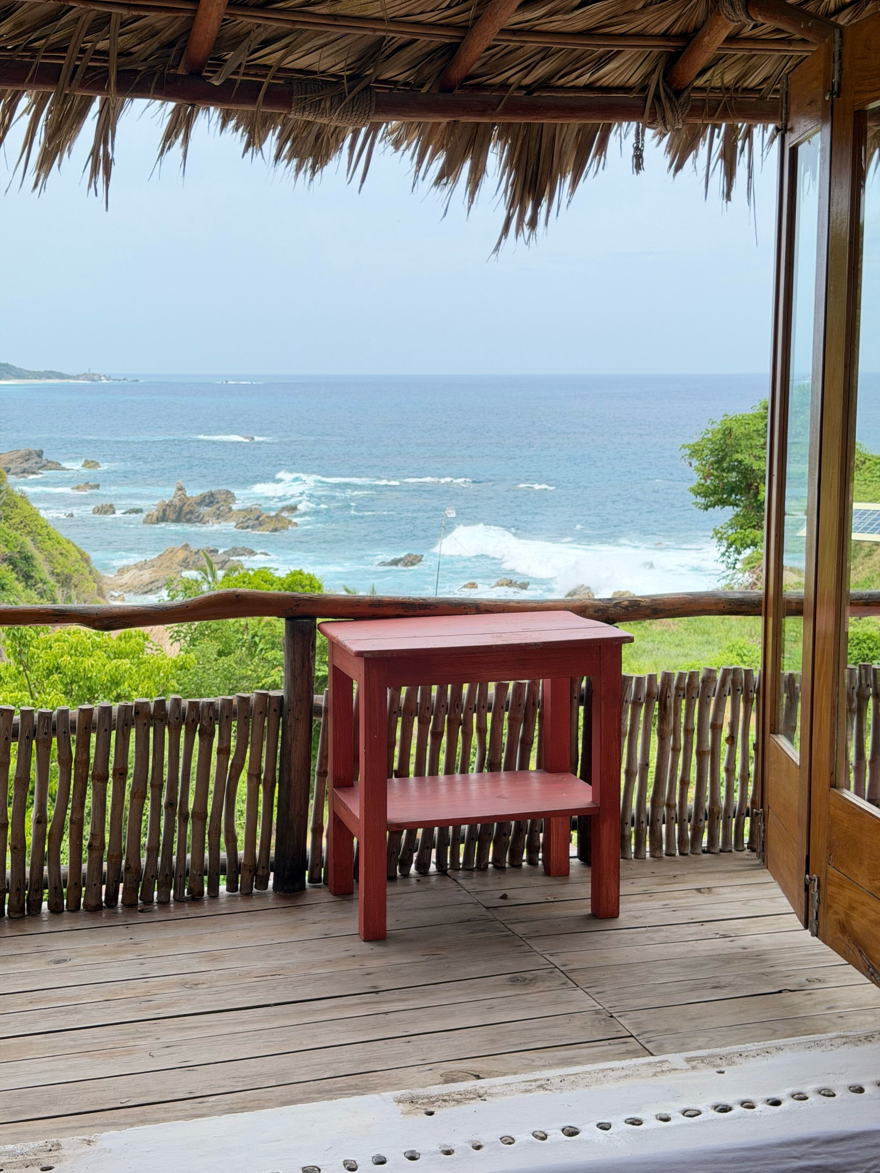 A wooden deck with a red table, overlooking a rocky coastline and ocean.