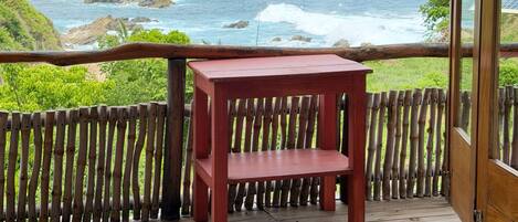 A wooden deck with a red table, overlooking a rocky coastline and ocean.