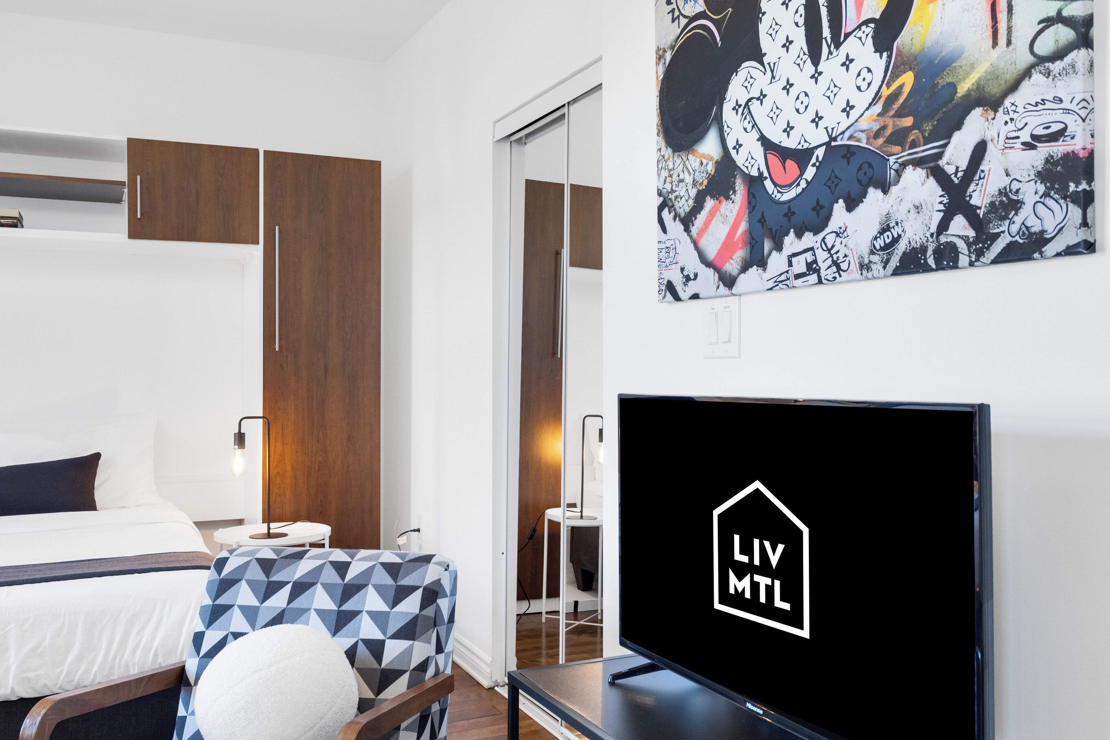A modern hotel room with a bed, a TV, and a large abstract painting on the wall.