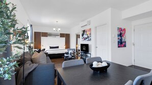 A modern living room with a sofa, dining table, and a TV. There is a plant, a painting, and a door in the background. - LiV MTL - MTL (Montreal)