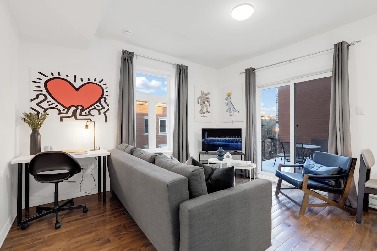 A modern living room with a grey sofa, a black office chair, a dining table, and a TV.
