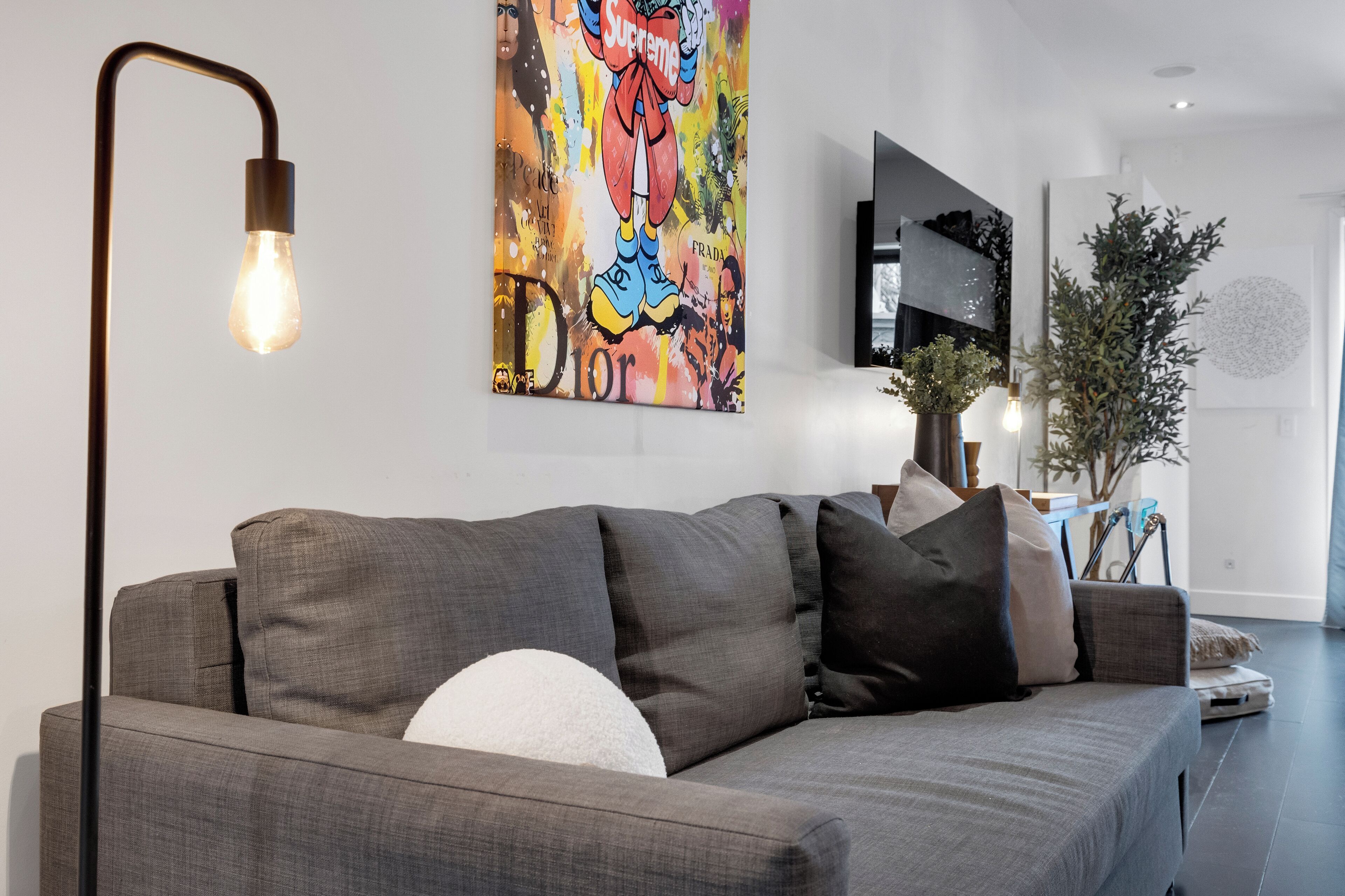 A modern living room with a grey sofa, a floor lamp, and a colorful abstract painting on the wall.