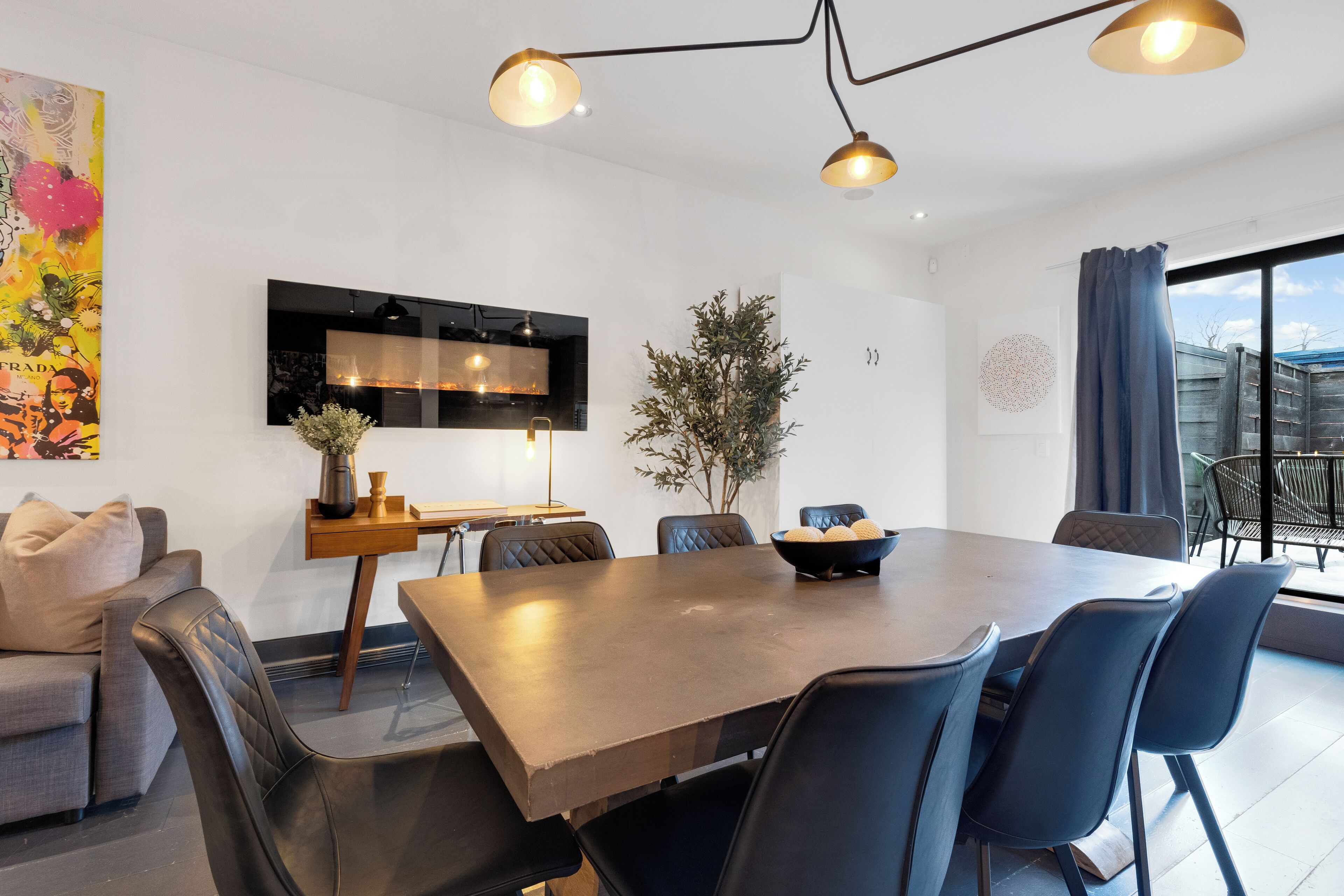 Un comedor moderno con una mesa grande, sillas negras e iluminación colgante.