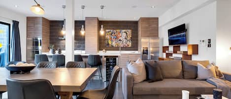 Un salon moderne comprenant un canapé, une table à manger et des chaises. Il y a également un coin cuisine avec un réfrigérateur et un four.
