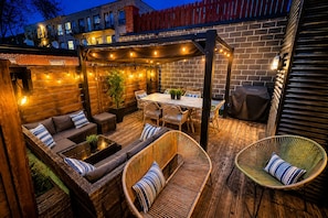 Un espace extérieur aménagé en terrasse, avec une plateforme en bois, des meubles en osier, une table à manger et des guirlandes lumineuses.