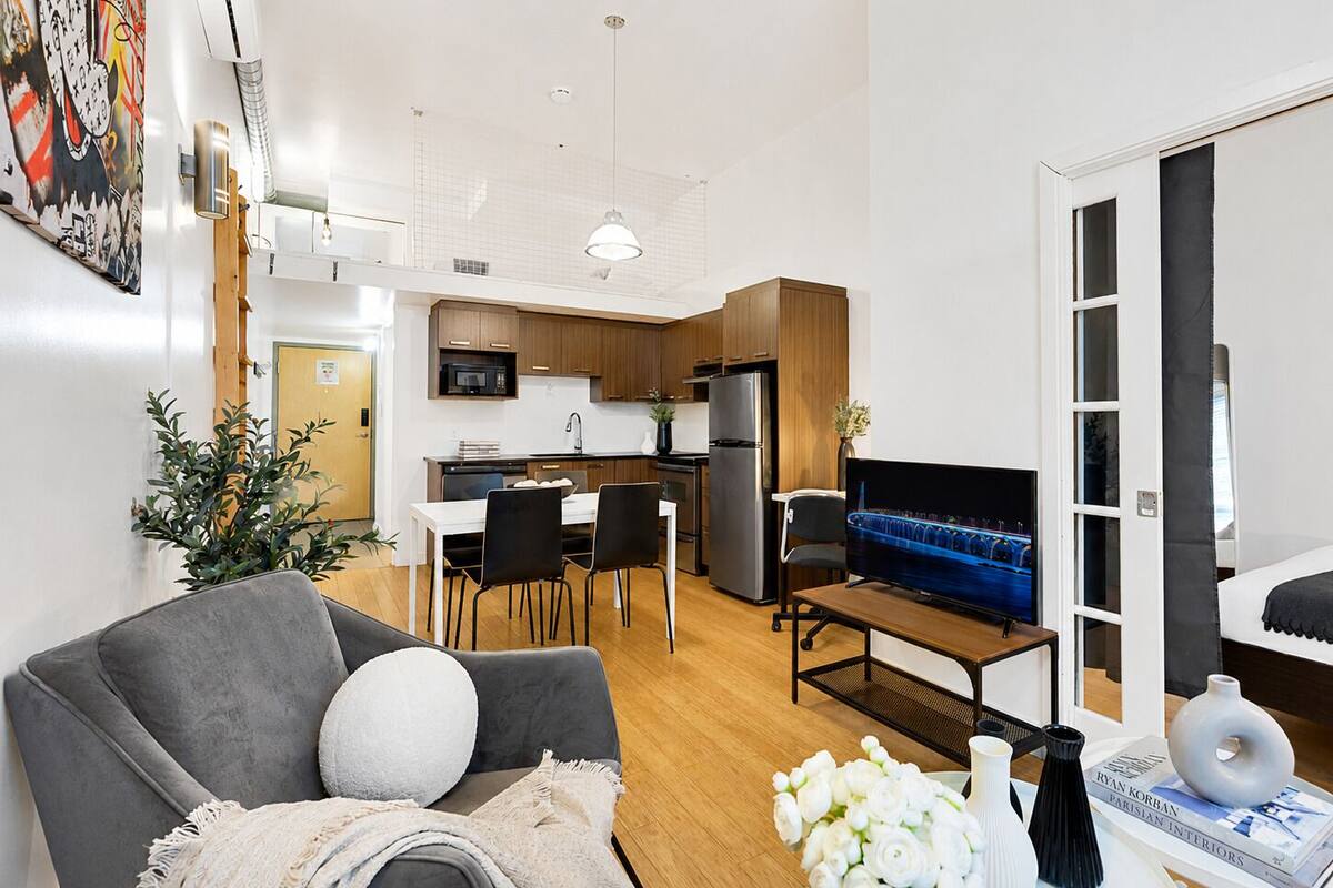 Una sala de estar moderna con un sofá gris, un televisor de pantalla plana y un comedor con una mesa y sillas blancas.