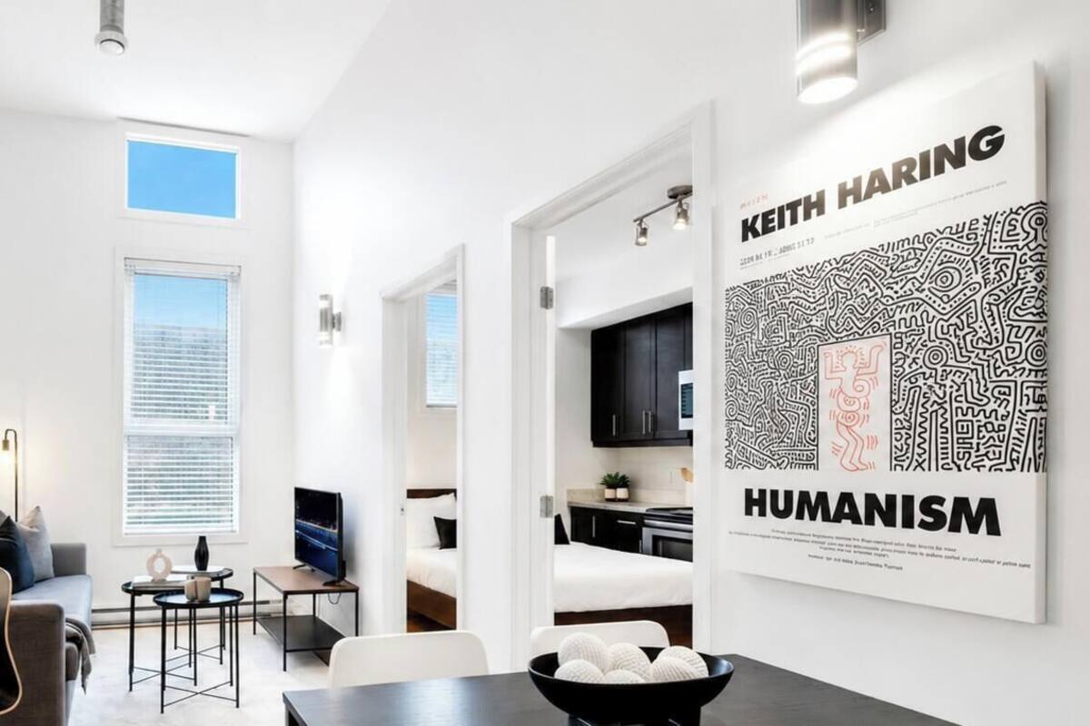 Un interior moderno con comedor, cocina y sala de estar, que incluye obras de arte y un cartel grande.