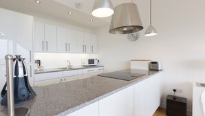 A modern kitchen with white cabinets, granite countertops, stainless steel appliances, and pendant lighting.
