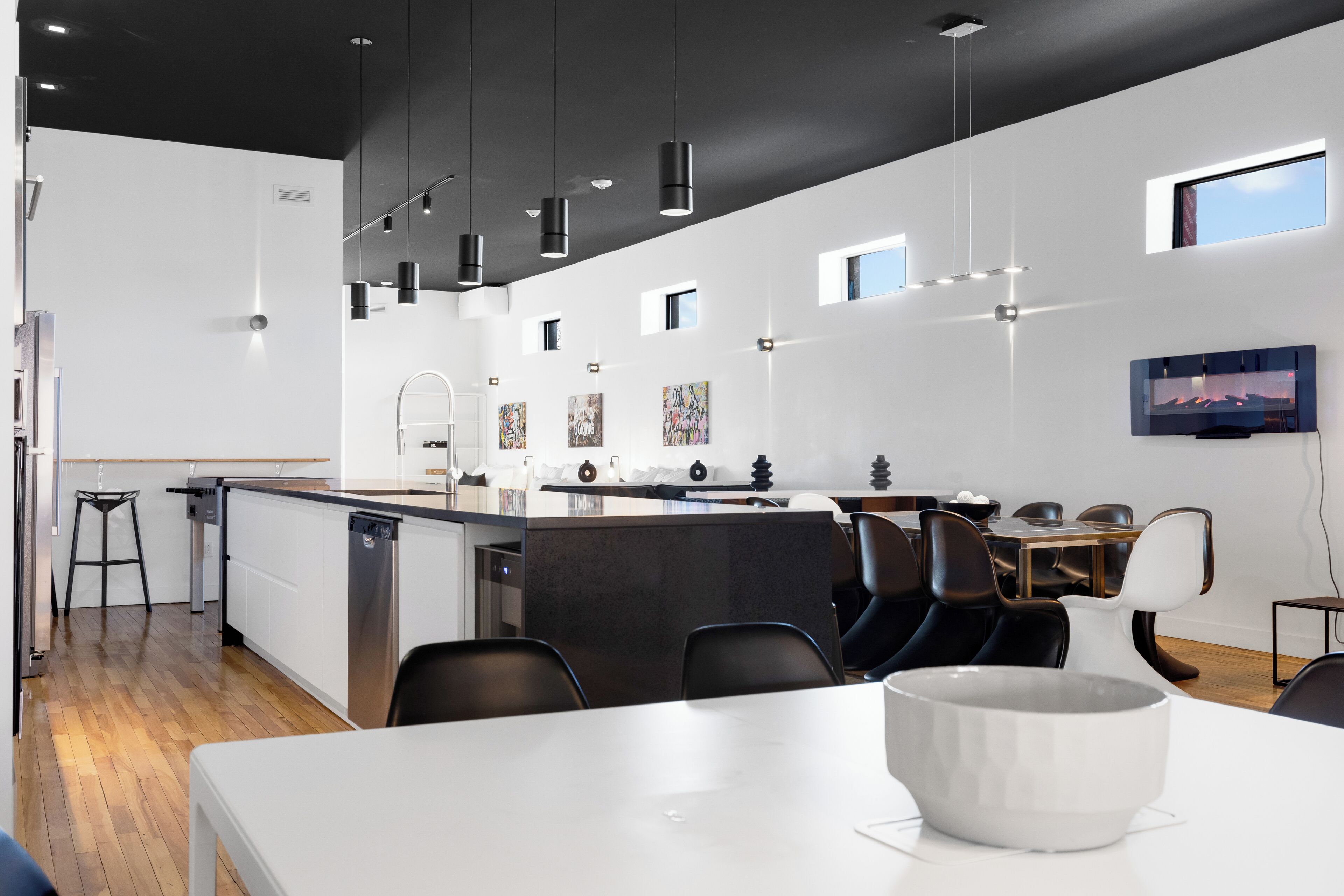 A modern kitchen with a central island, pendant lighting, and a dining area with chairs and a table.
