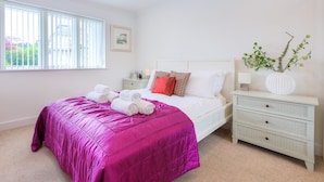A bedroom with a bed, a nightstand, a dresser, a window with blinds, and a vase with greenery. - Indigo (St Ives)