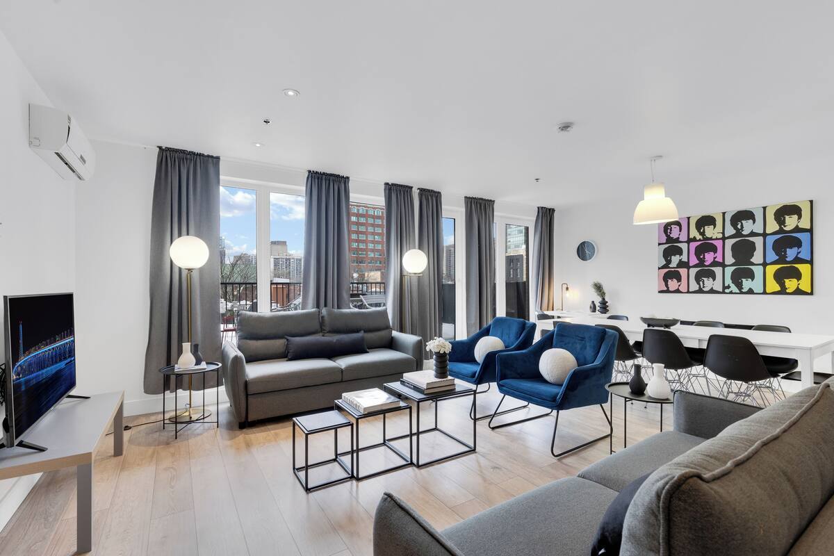 A modern living room with a grey sofa, blue armchairs, and a flat-screen TV.