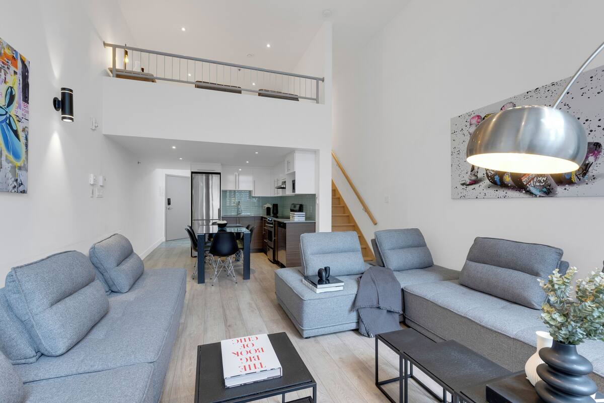 A modern living room with grey sofas, a black coffee table, and a staircase leading to an upper level.