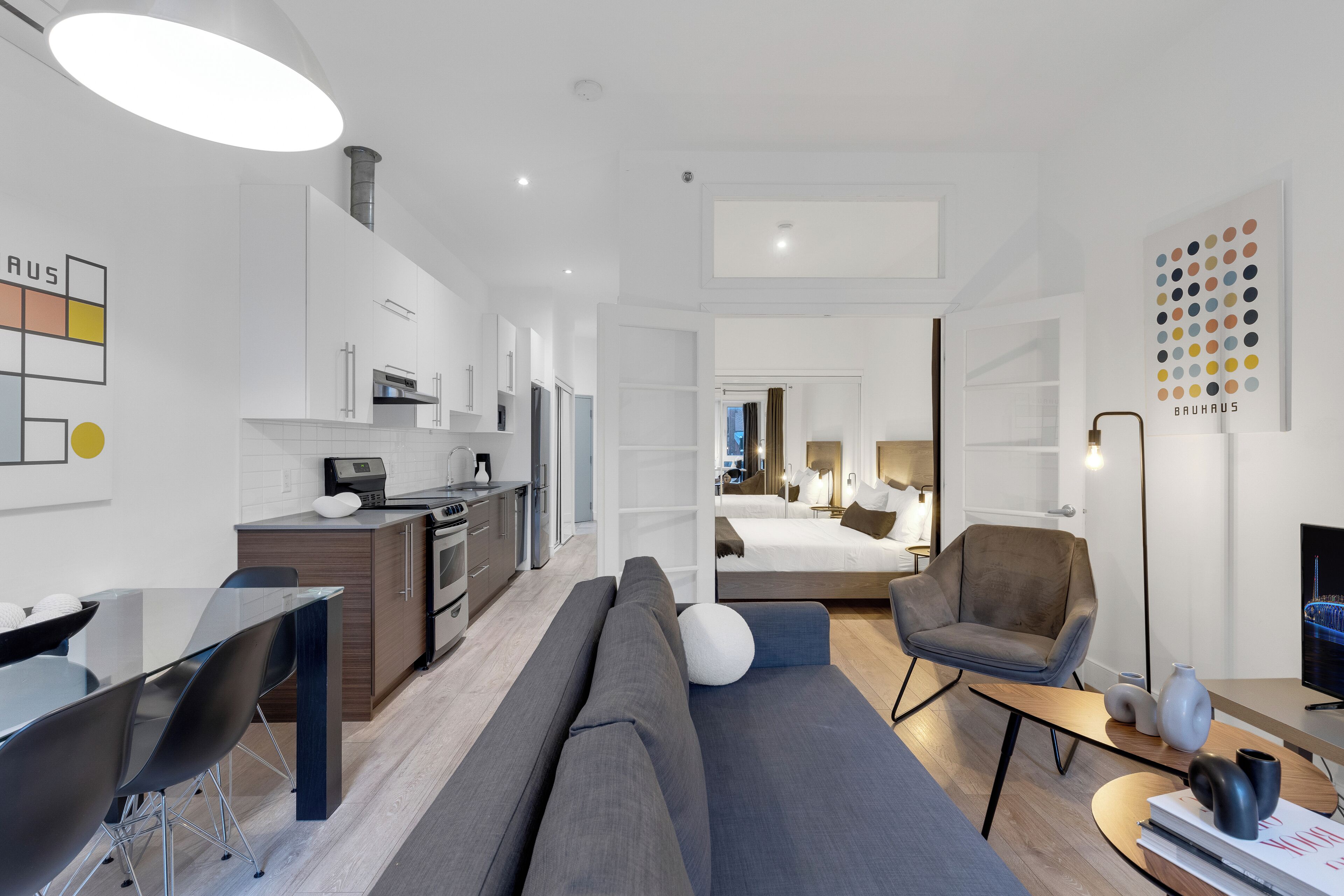 Una camera d'hotel moderna con angolo cottura, divano, poltrona, scrivania e letto.