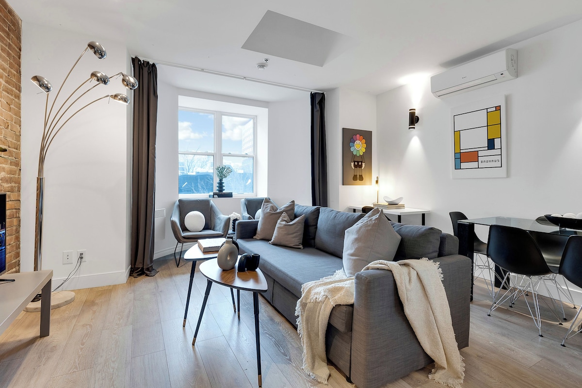 A modern living room with a grey sofa, a coffee table, and a dining area with a black chair.