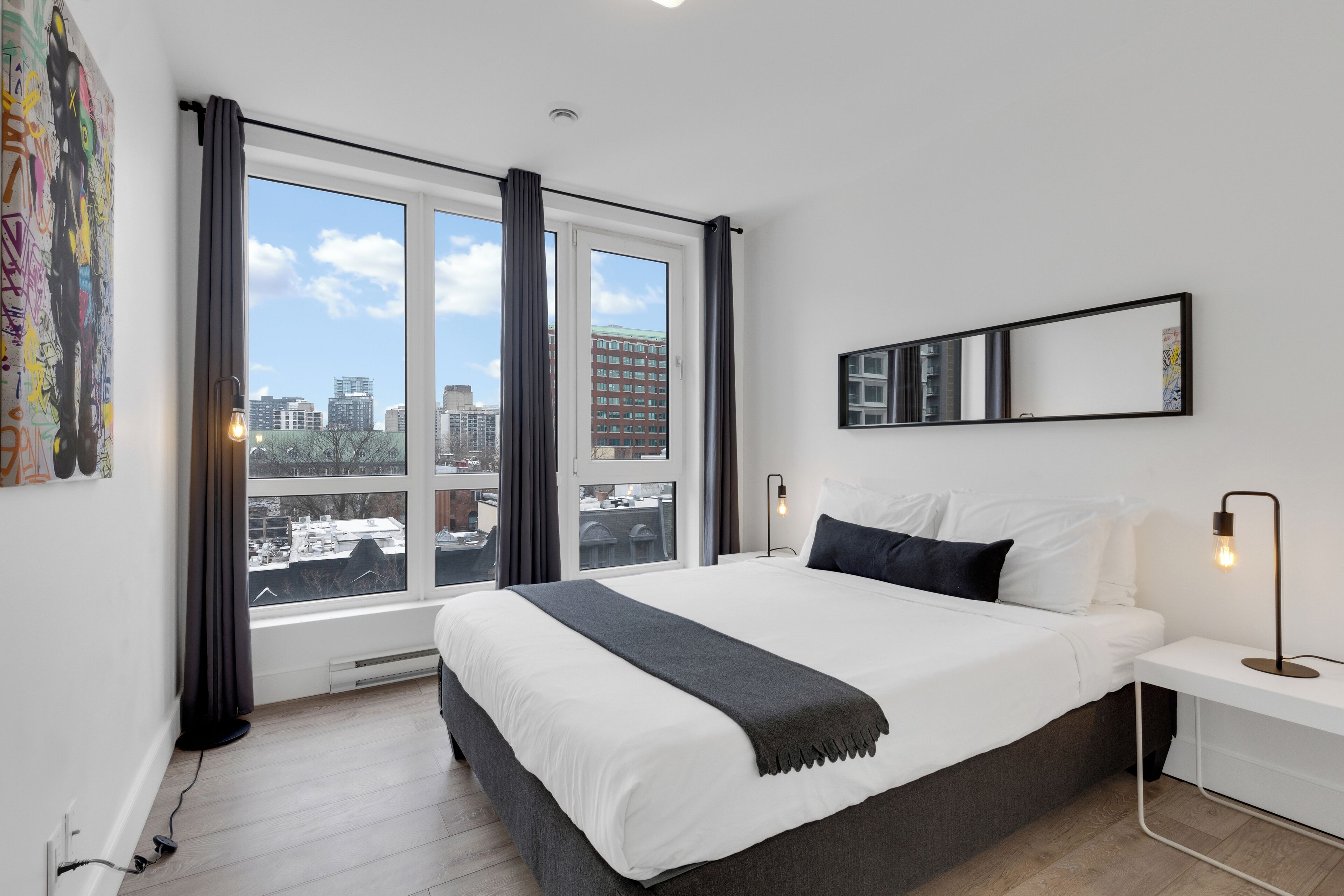Une chambre d’hôtel moderne, dotée d’un grand lit, offrant une vue sur le paysage urbain et présentant une décoration minimaliste.