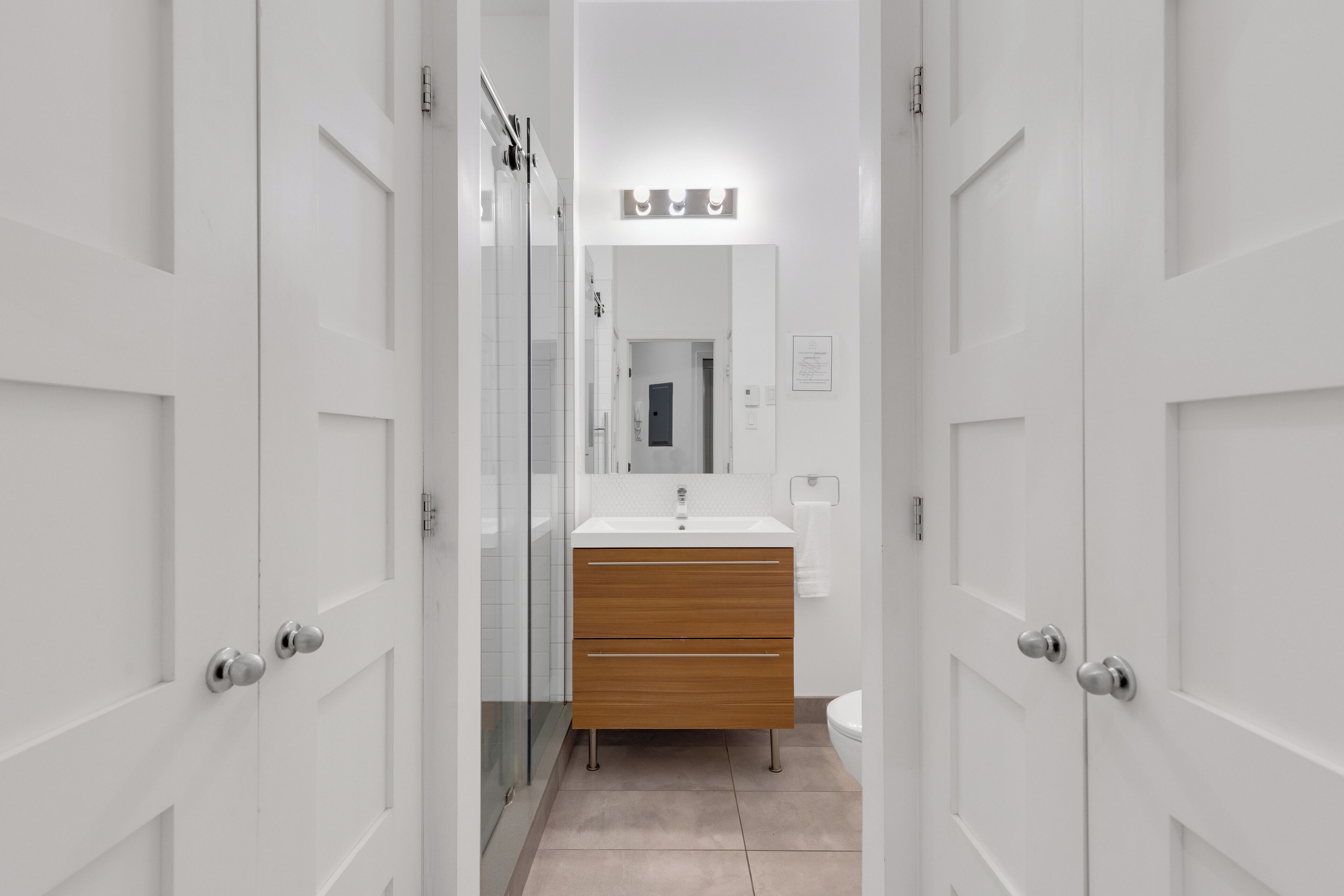 Une salle de bain moderne avec une douche en verre, des meubles blancs et un meuble-lavabo en bois.