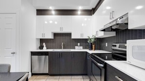 Une cuisine moderne avec des meubles blancs, un pare-feu noir et des appareils électroménagers en acier inoxydable.