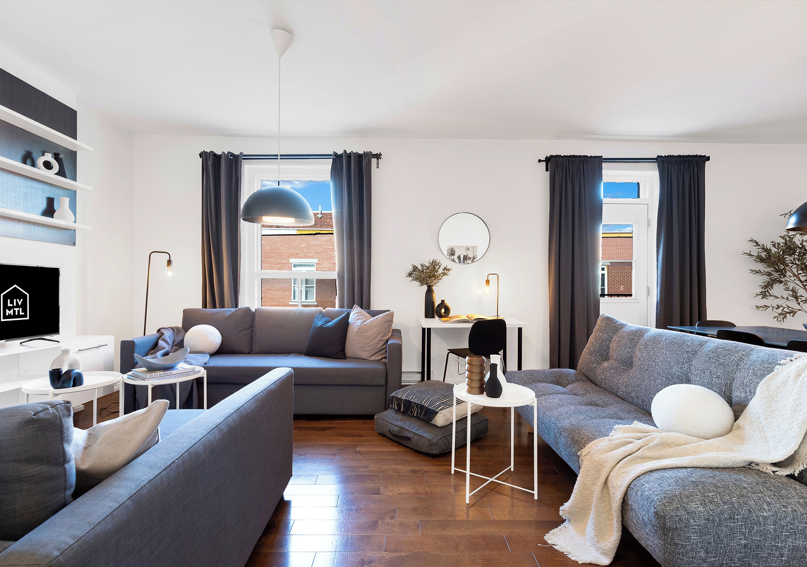Una sala de estar moderna con un sofá gris, un sofá gris más pequeño, una mesita de noche blanca y una estantería.