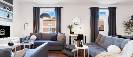Una sala de estar moderna con un sofá gris, un sofá gris más pequeño, una mesita de noche blanca y una estantería.