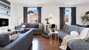 Un salon moderne avec un canapé gris, une table basse blanche et un téléviseur posé sur un meuble.