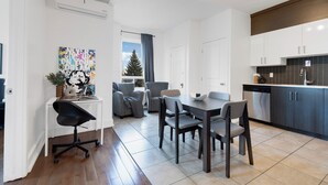 Une cuisine moderne avec des meubles de couleur sombre, un coin repas avec une table et des chaises, et une vue sur un arbre à l’extérieur.