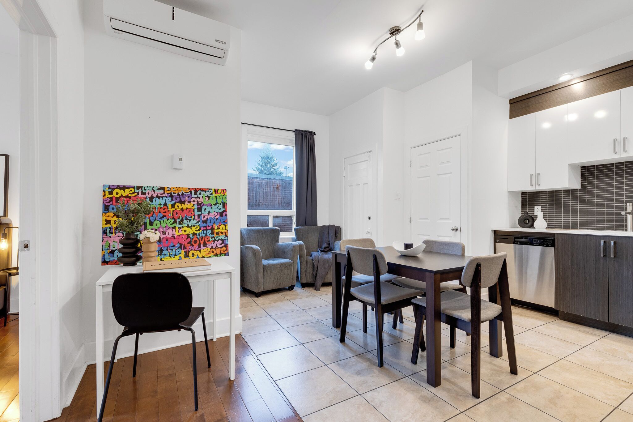 A modern kitchen with white cabinets, a dining area with a table and chairs, and a colorful wall art piece.