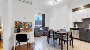 A modern kitchen with white cabinets, a dining area with a table and chairs, and a colorful wall art piece.
