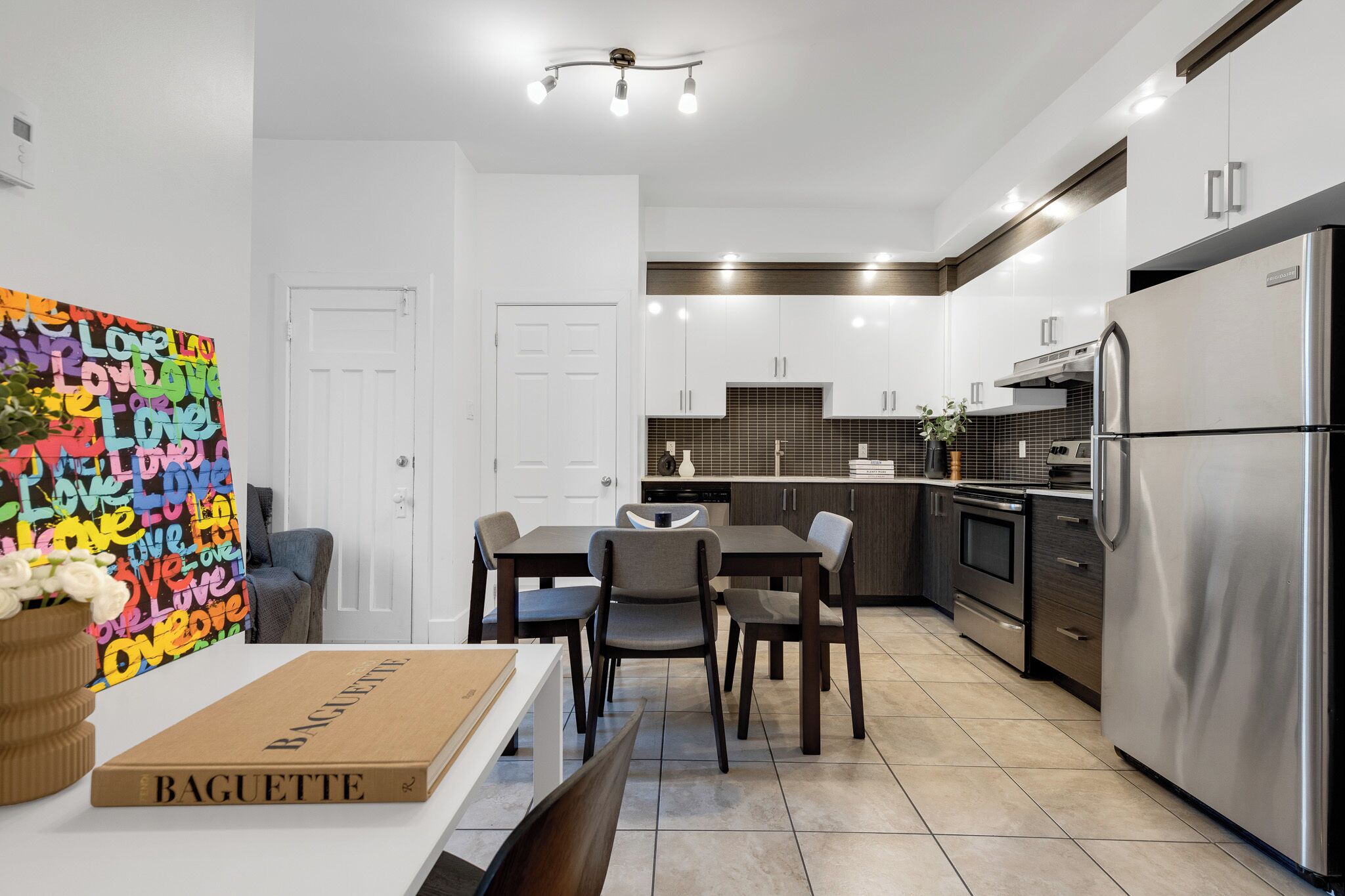 A modern kitchen with a dining area, stainless steel appliances, and a colorful abstract painting on the wall.