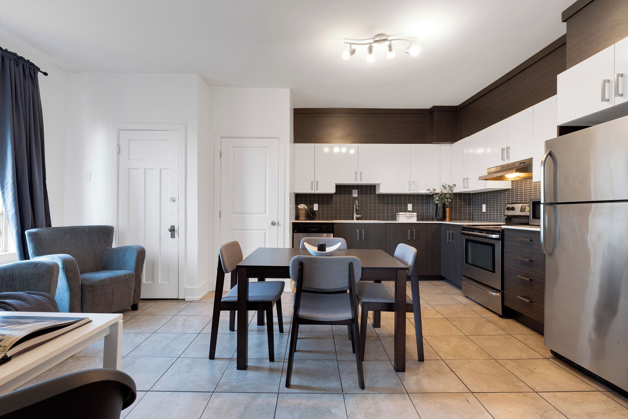 Una cocina moderna con armarios oscuros, un refrigerador de acero inoxidable y una zona de comedor con una mesa y sillas.