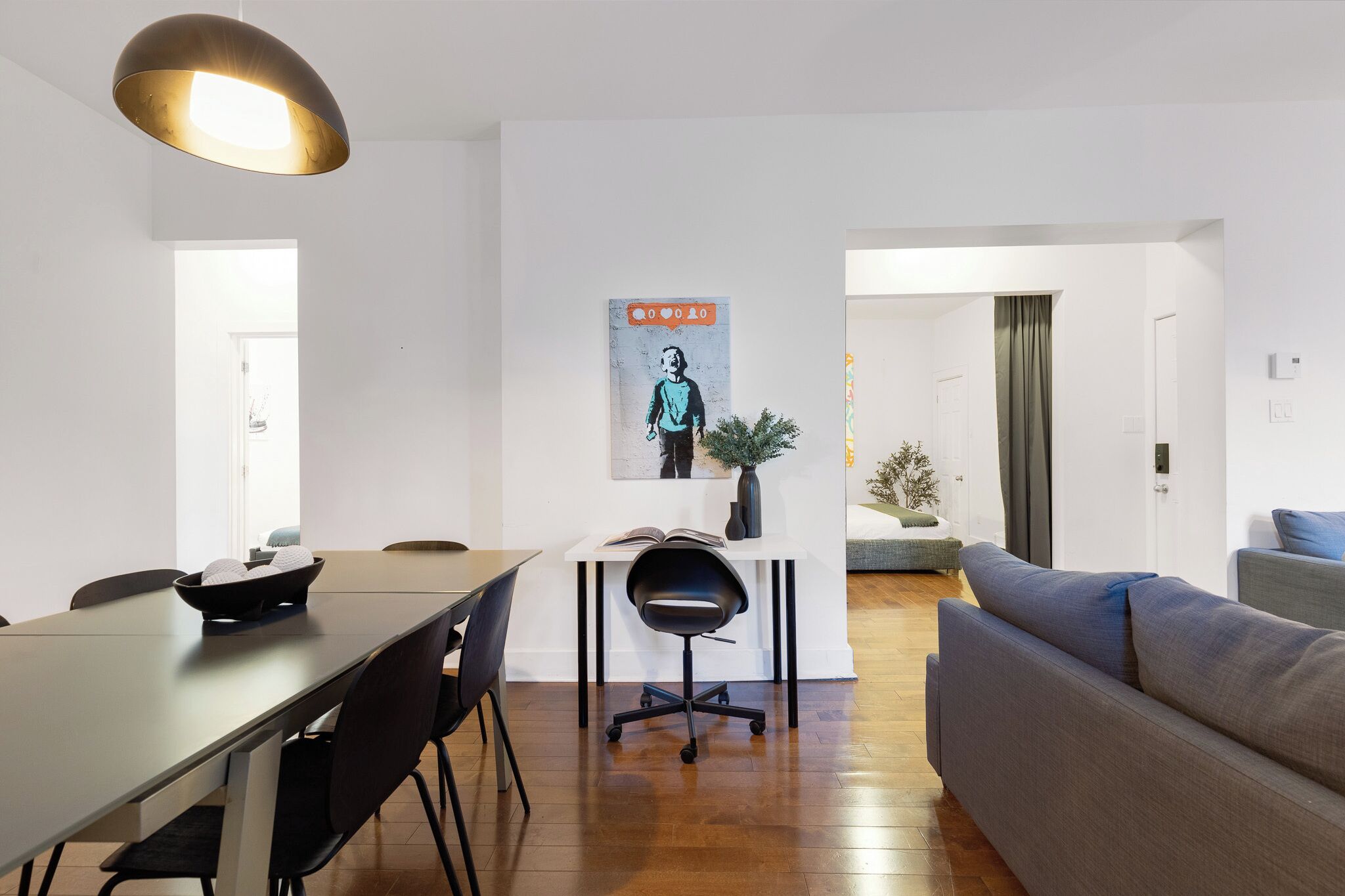Un salon moderne avec un canapé, une table à manger et des chaises, un luminaire suspendu et une affiche au mur.