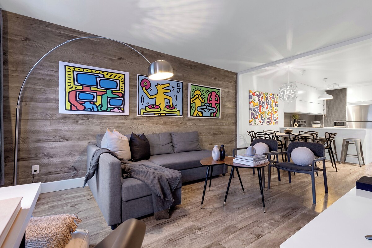 A modern living room with a grey sofa, a coffee table, and a dining area with chairs and a table.