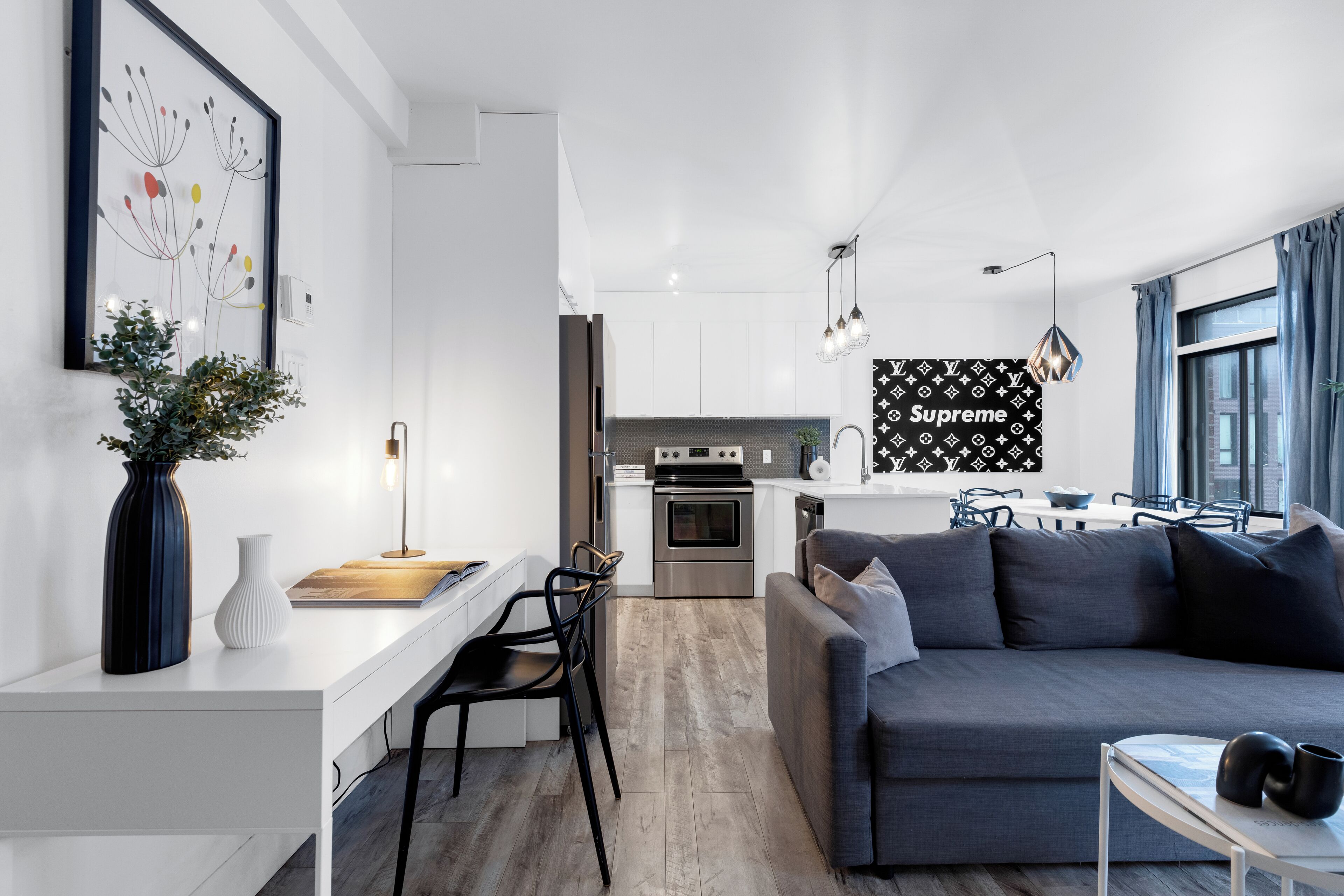 Een moderne keuken met witte kasten, een inbouwoven en een zithoek met een grijze bank en een kleine tafel.