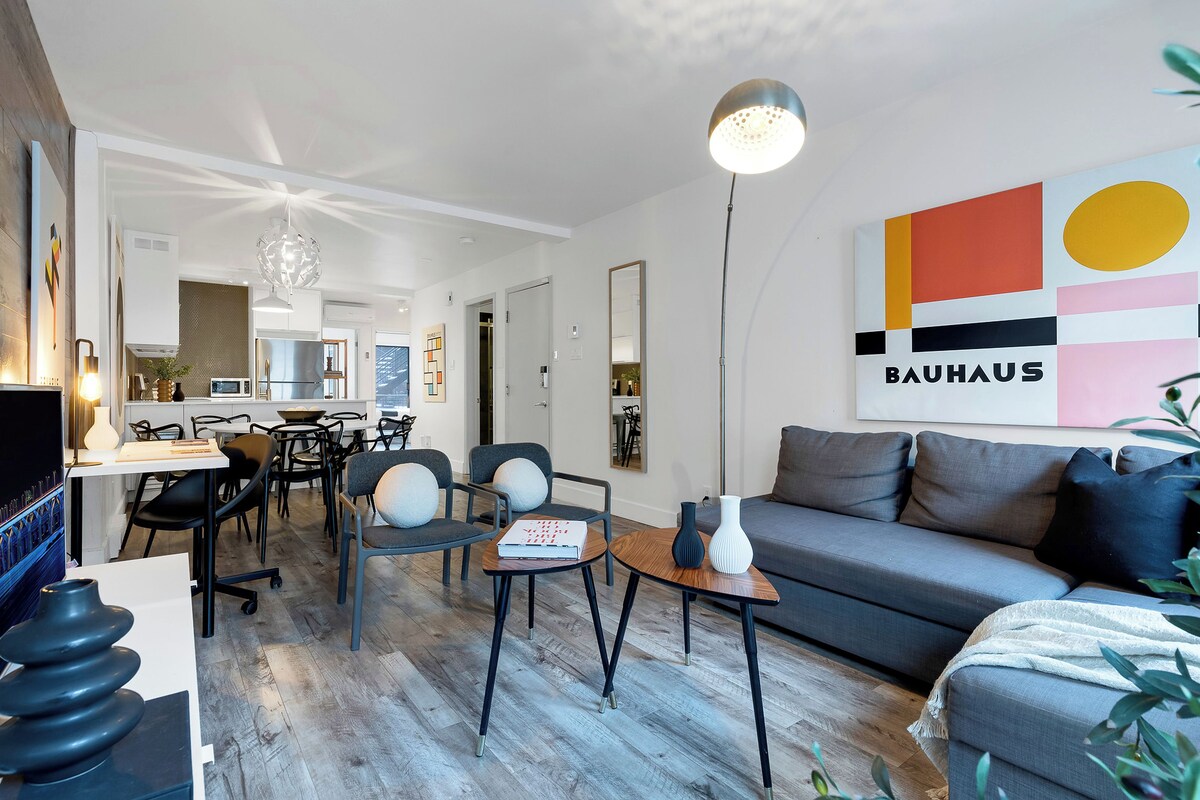 A modern living room with a sofa, chairs, a dining area, and a kitchen in the background.