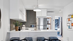 A modern kitchen with a central island, stainless steel appliances, and a dining area with a marble table and chairs. - LiV MTL - Urban (Montreal)