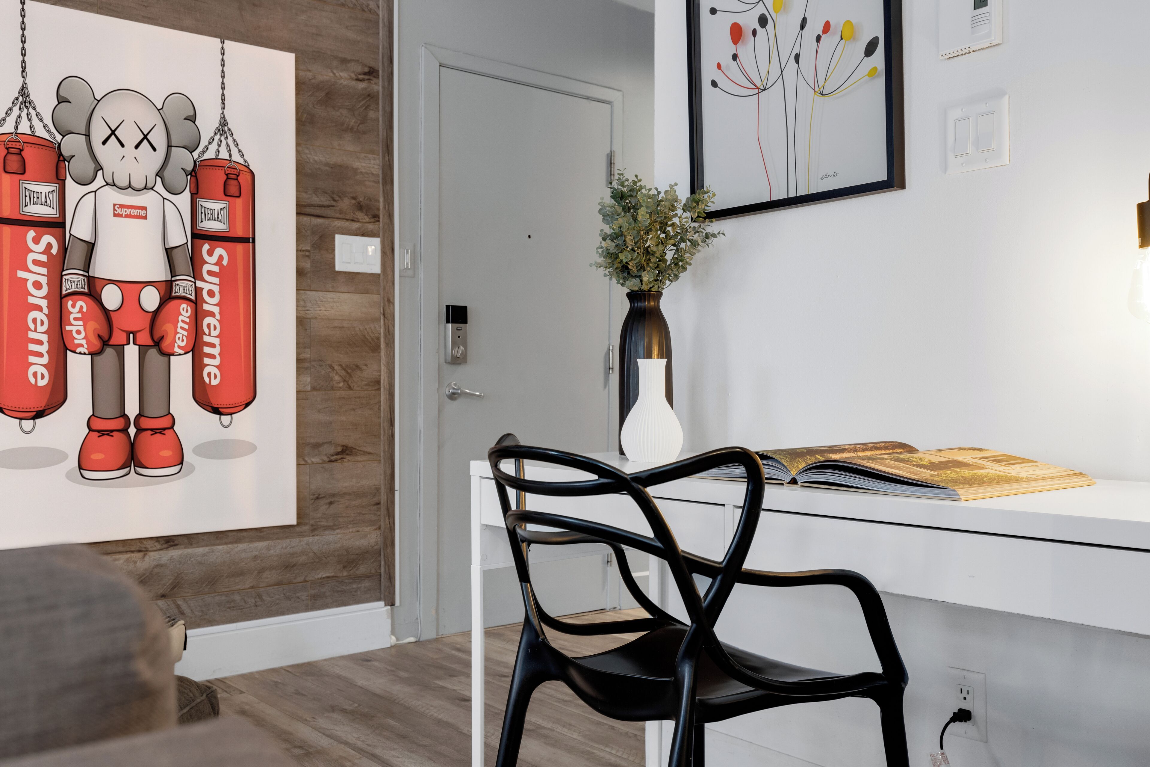 A modern room with a white desk, a black chair, a framed artwork, and a vase with plants.