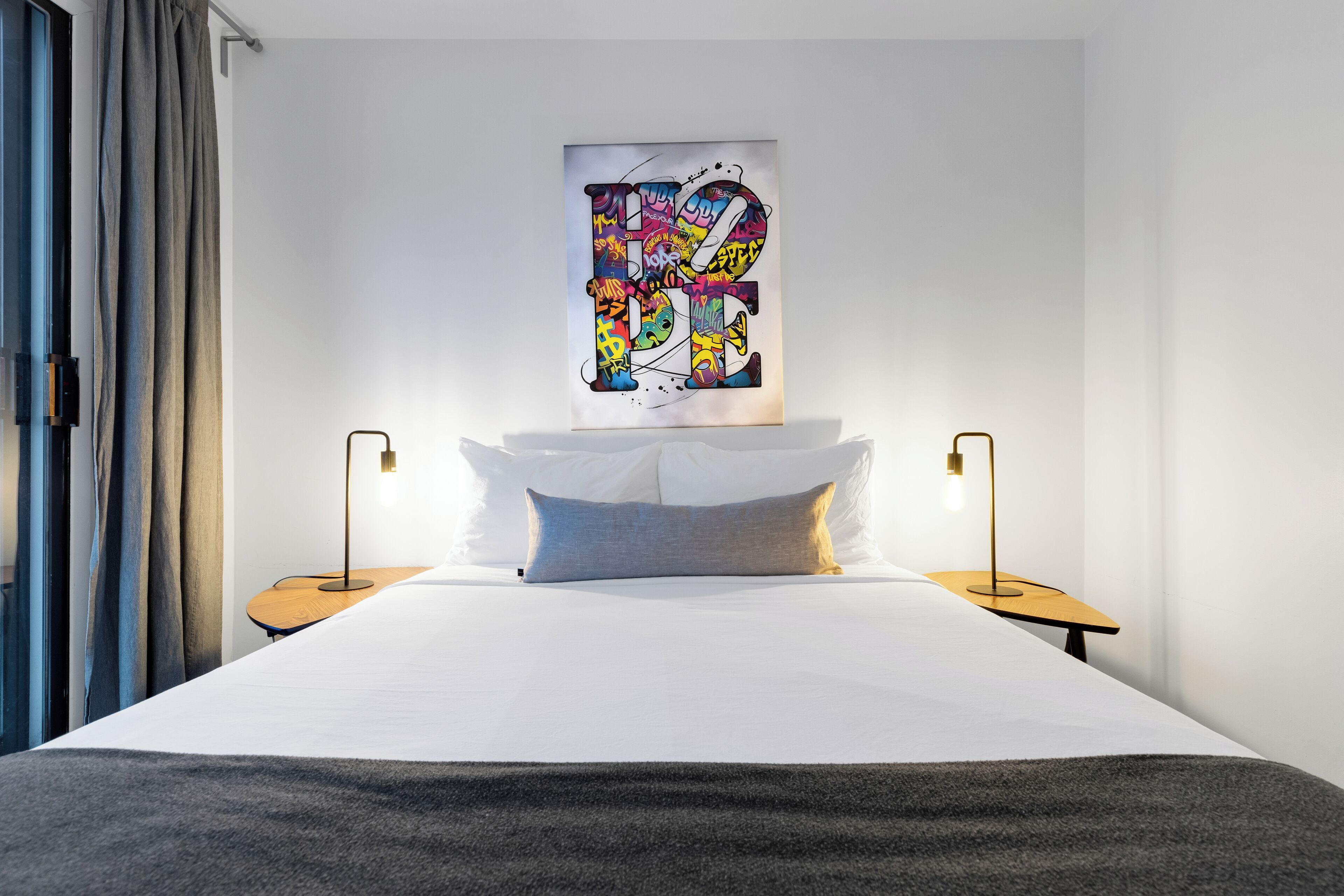 Una camera d'hotel moderna con un letto grande, due comodini e un'opera d'arte astratta dai colori vivaci appesa al muro.