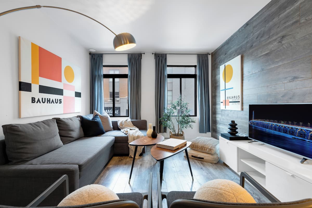 Een moderne woonkamer met een grijze bank, een bijzettafeltje, een televisie en kunstwerken aan de muur.
