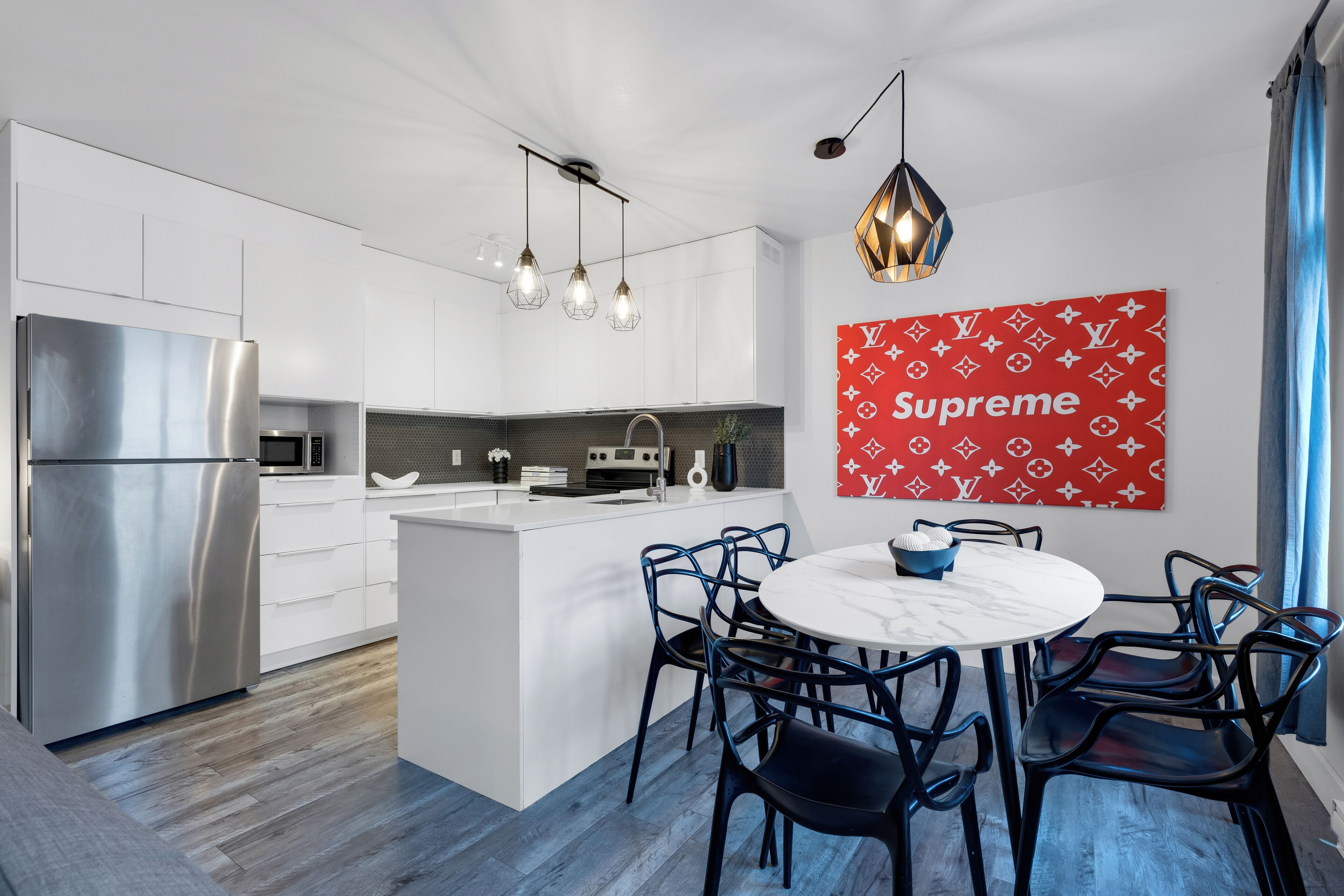 Una cocina moderna con una isla central, electrodomésticos de acero inoxidable, iluminación colgante y una obra de arte mural roja de Louis Vuitton 'Supreme'.
