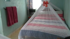 A room with a bed under a mosquito net, a chair, a table, and a window with curtains. - Usenge Sunset Resort (Usenge)