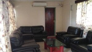 A living room with black leather sofas, a glass coffee table, and a red accent table. There is a door in the background and a window with curtains. - Usenge Sunset Resort (Usenge)
